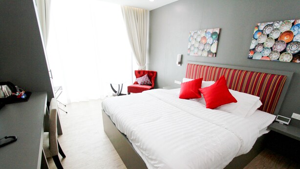 A modern hotel room with a large bed, a red chair, and a wall decorated with plates. - Coco at 20 (Bangkok)