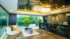 A modern lobby with a reception desk, seating area, and a large glass wall with a view of greenery. - Serenity Condo Wongamat by Patsamon (Pattaya)