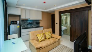 A modern living room with a sofa, a TV, and a kitchen area with cabinets and a microwave. - Serenity Condo Wongamat by Patsamon (Pattaya)