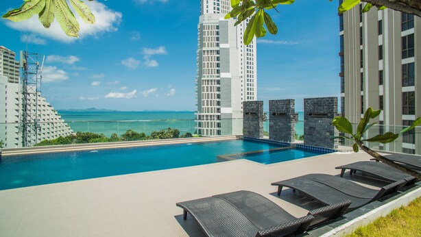 A rooftop pool with lounge chairs, a view of the ocean, and high-rise buildings in the background. - Serenity Condo Wongamat by Patsamon (Pattaya)