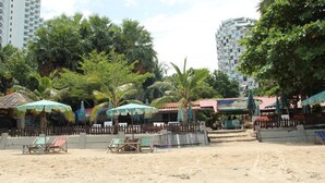 A beach with several umbrellas, lounge chairs, and a fence. - Serenity Condo Wongamat by Patsamon (Pattaya)
