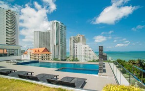 A rooftop pool with lounge chairs, surrounded by high-rise buildings and a clear view of the ocean.