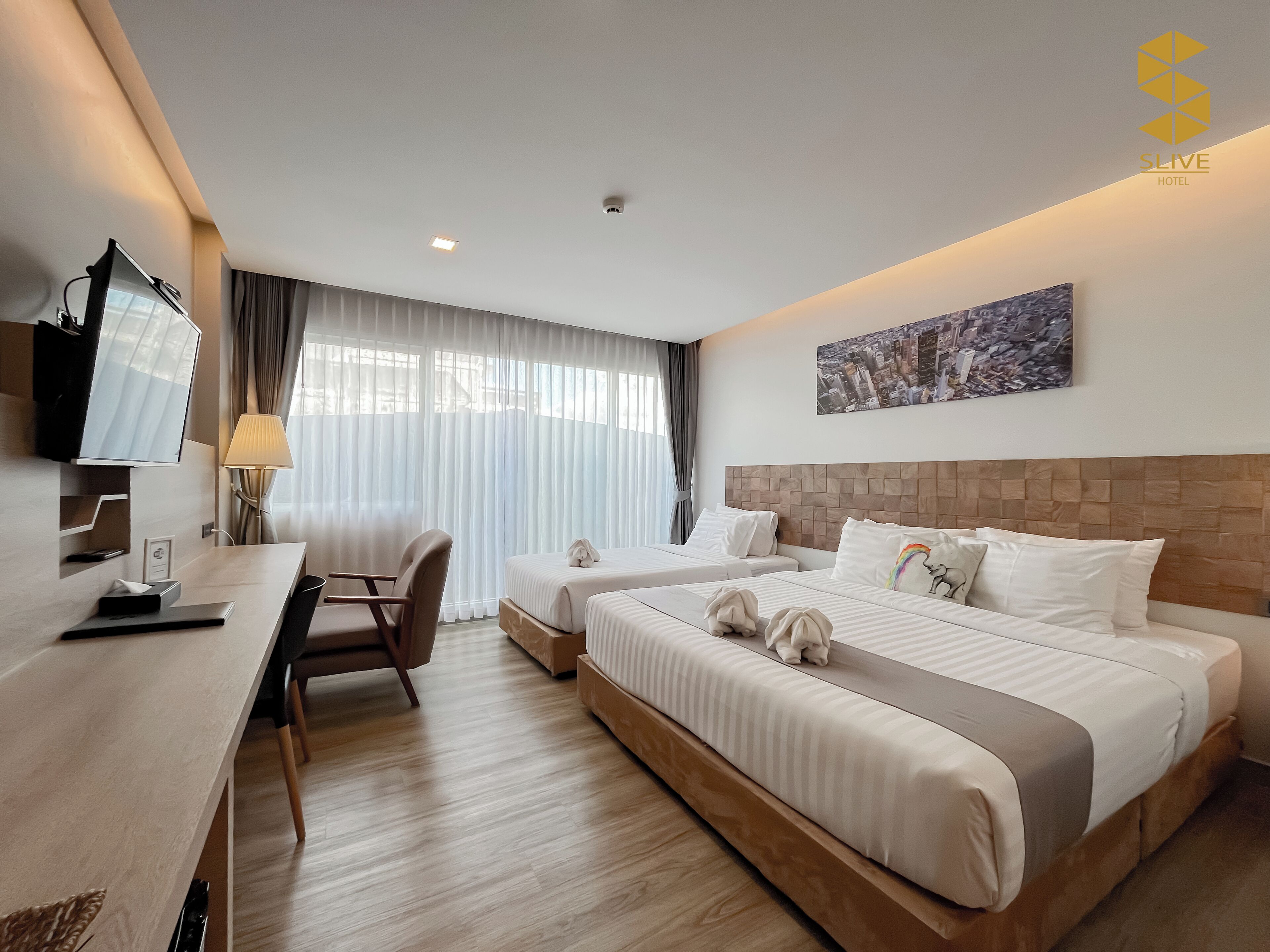A hotel room with two beds, a desk, a chair, a TV, and a window with curtains.