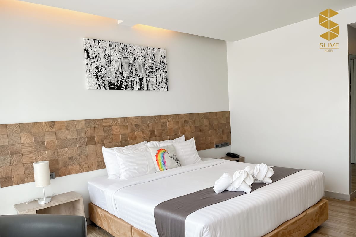 Ein Hotelzimmer mit Bett, Nachttisch, Lampe, Wandbild und einem Logo an der Wand.