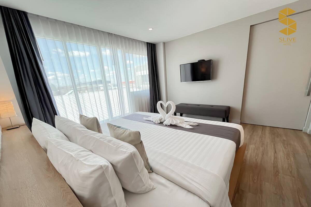 Ein Hotelzimmer mit einem großen Bett, einem Fernseher an der Wand und Blick ins Freie.