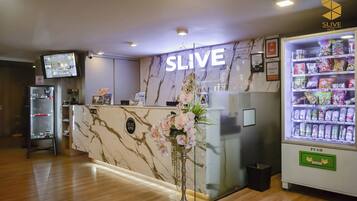 A hotel reception area with a marble counter, a floral centerpiece, a television, and a vending machine.