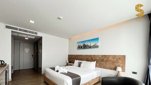 A modern hotel room with a large bed, a wooden headboard, a cityscape painting, a desk with a lamp, and a chair.