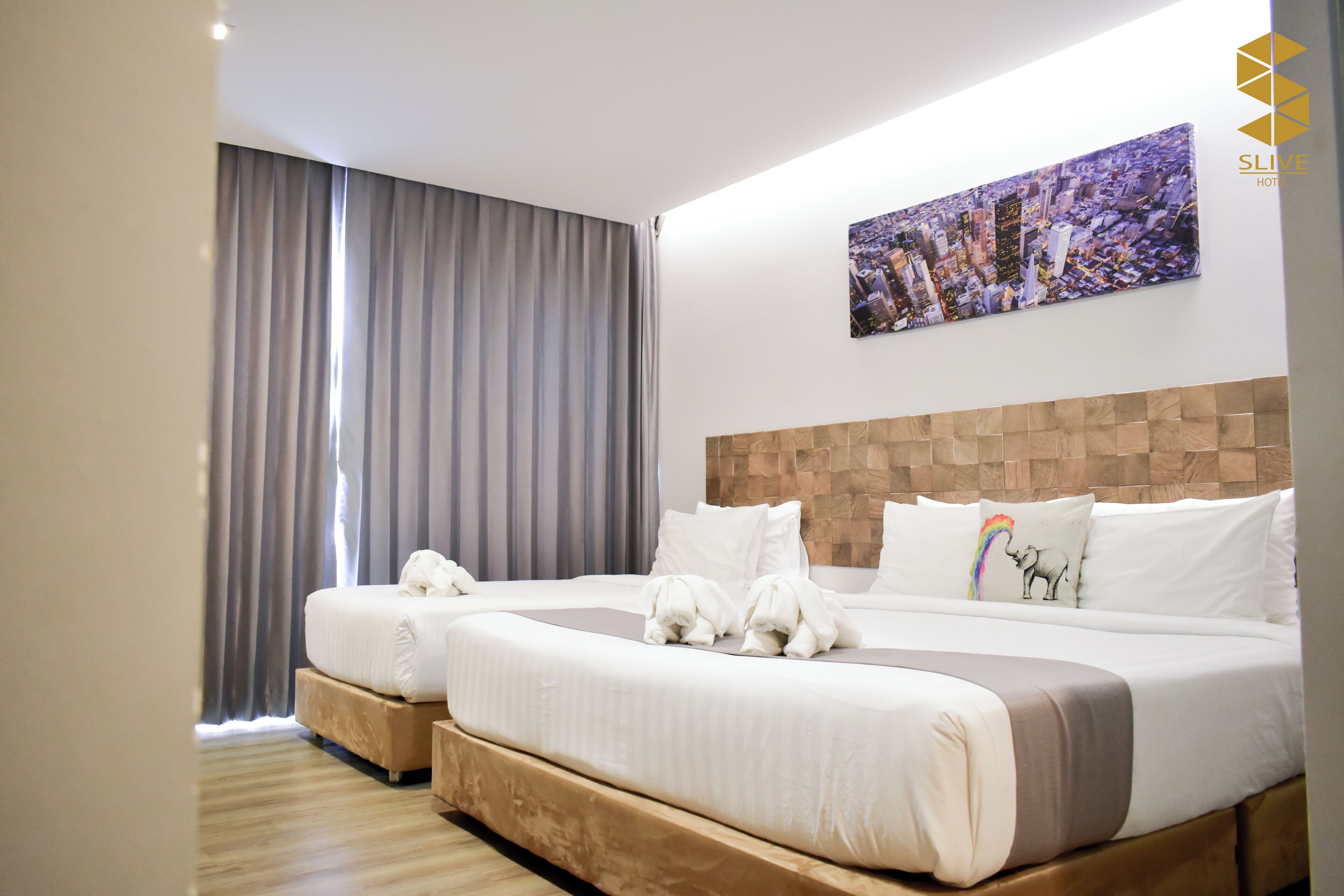 A hotel room with two beds, a cityscape painting, and a large window with curtains.