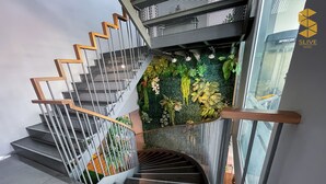 A modern staircase with a wooden handrail, metal railings, and a green wall with plants.