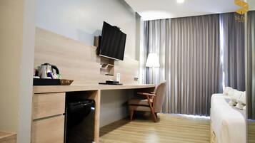 A hotel room with a wooden desk, a television, a chair, a bed, and a window with curtains.