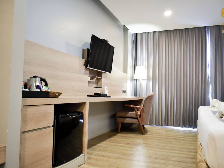 A hotel room with a wooden desk, a television, a chair, a bed, and a window with curtains.