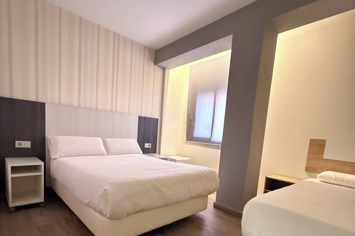 A modern hotel room with a large bed, a bedside table, and a small bedside table.