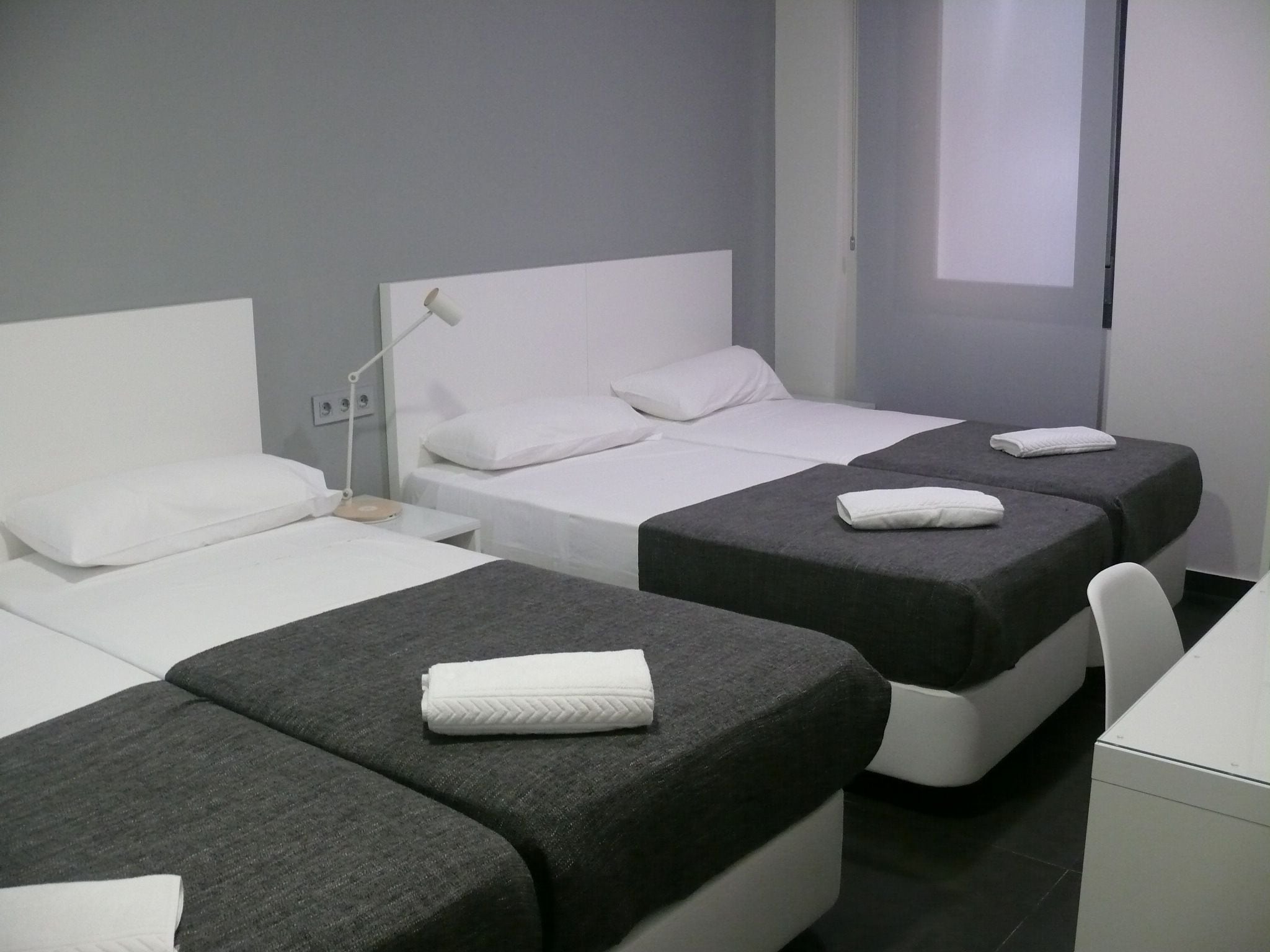 A hotel room with two single beds, a desk, and a chair.