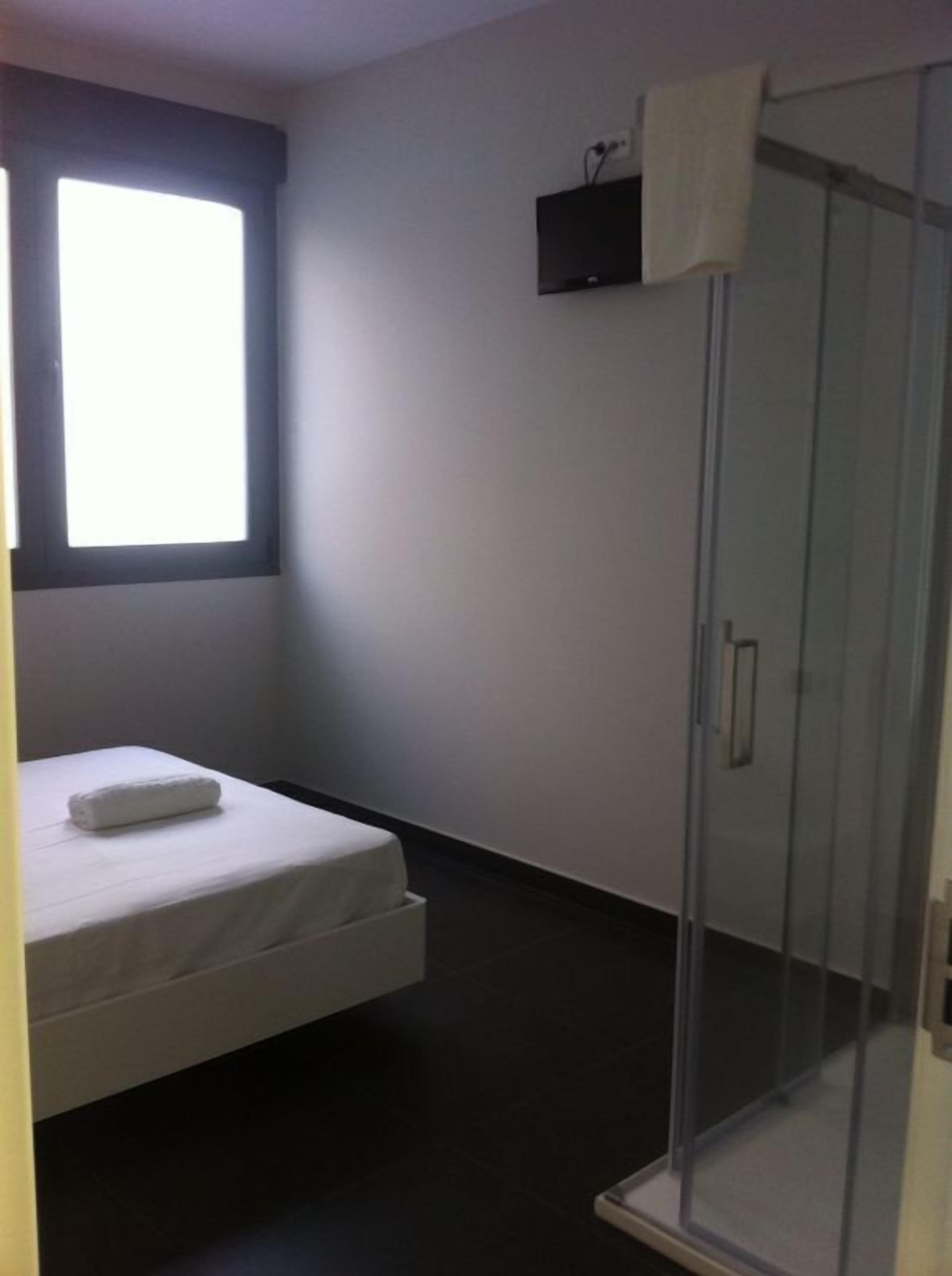 A small, modern room with a bed, a shower, and a window.