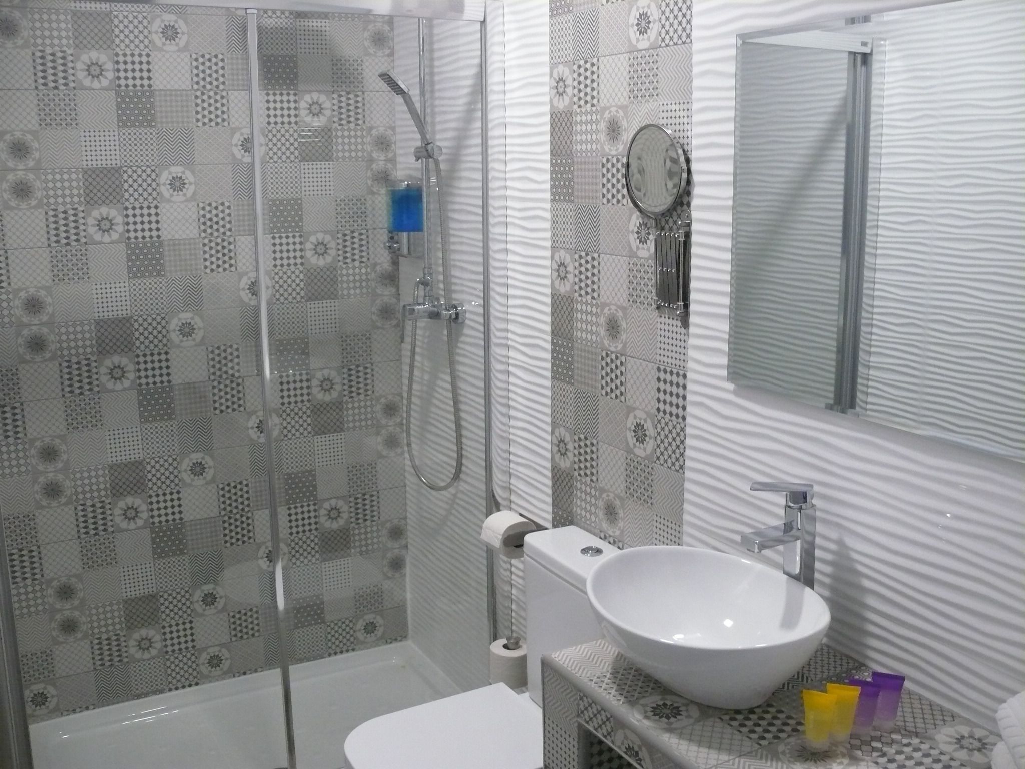 Un baño con mampara de vidrio, un lavamanos blanco y azulejos estampados.