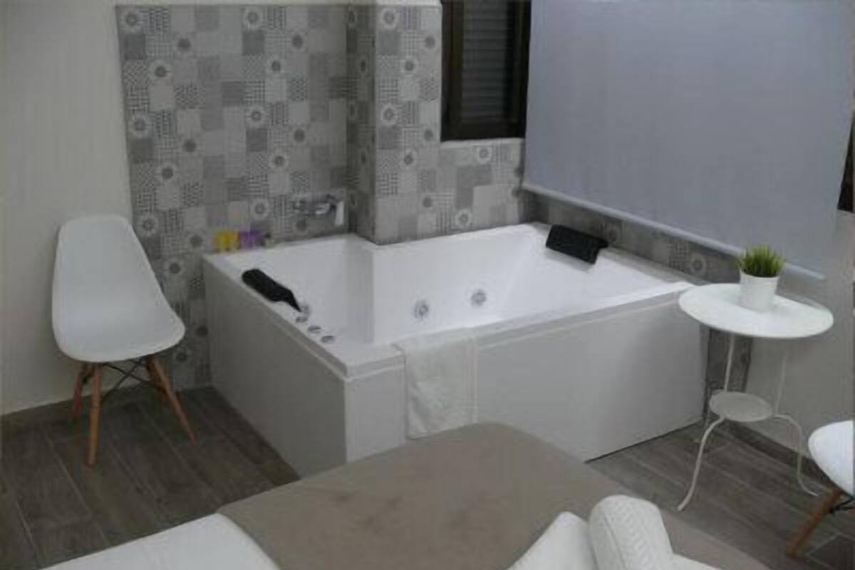 A modern bathroom with a large bathtub, a small white table with a plant, and a white chair.