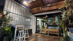 The exterior of Anna Hostel with a rustic wooden facade, a bench, and a small seating area with stools. - Lanna Hostel (Chiang Mai)