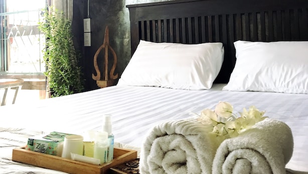 A neatly made bed with white linens, a wooden headboard, and a tray with toiletries. - Lanna Hostel (Chiang Mai)