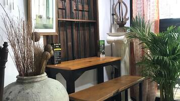 A rustic interior with a wooden table and bench, a large vase with dried plants, and a framed picture on the wall.