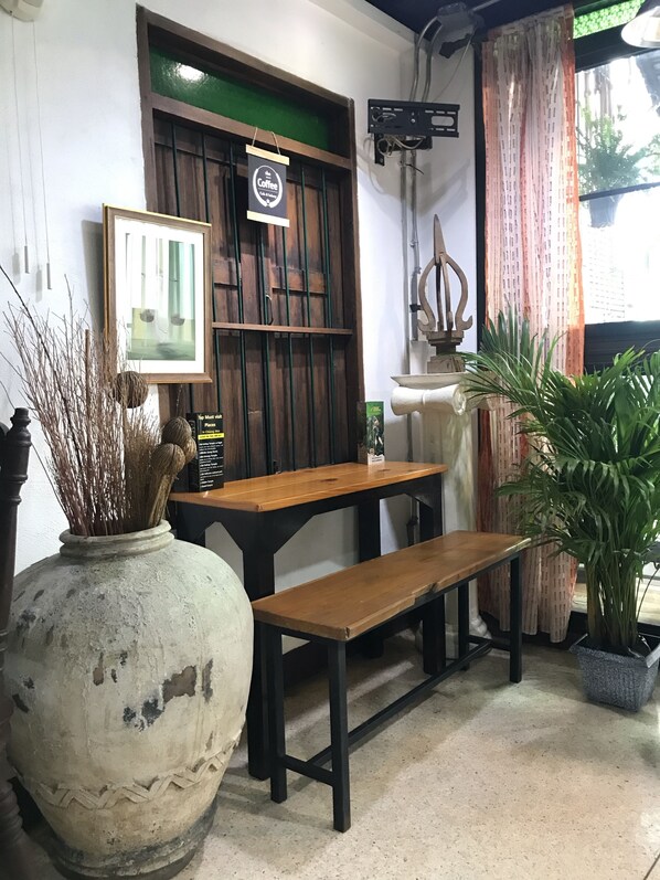 A rustic interior with a wooden table and bench, a large vase with dried plants, and a framed picture on the wall.