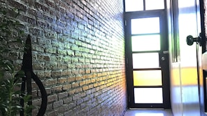 A hallway with a brick wall, a door with a frosted glass panel, and a plant on the left. - Lanna Hostel (Chiang Mai)