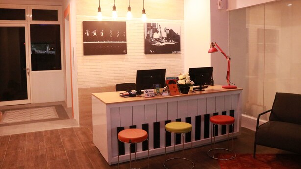 A reception desk with a computer, a telephone, and a small plant. There are three stools in front of the desk. - Front One Inn Semarang (Semarang)