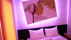 A hotel room with a bed featuring white bedding and pillows, a headboard, and a wall-mounted screen displaying a quote. - Front One Inn Semarang (Semarang)