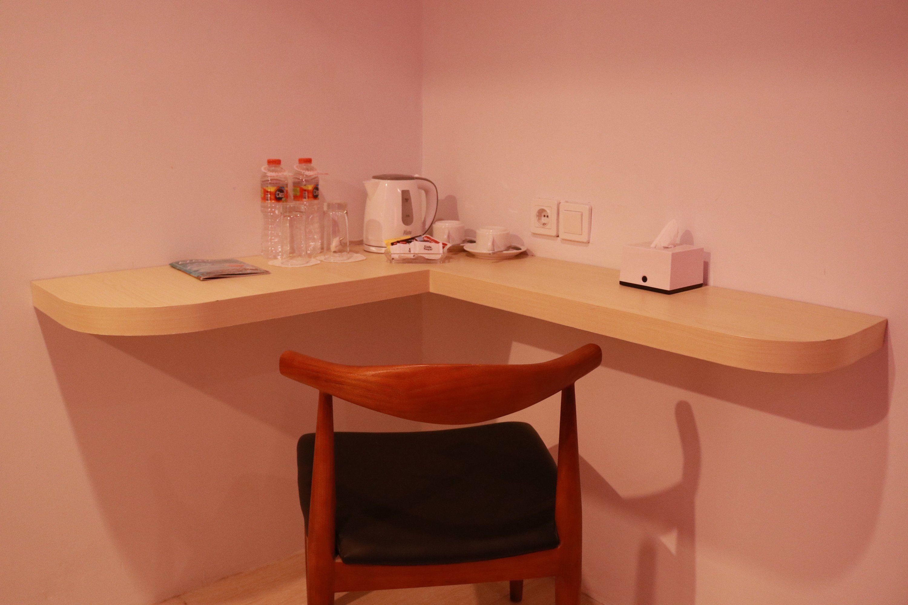 Ein Schreibtisch in der Ecke mit Stuhl, Wasserkocher, Tassen und einer Taschentuchbox.