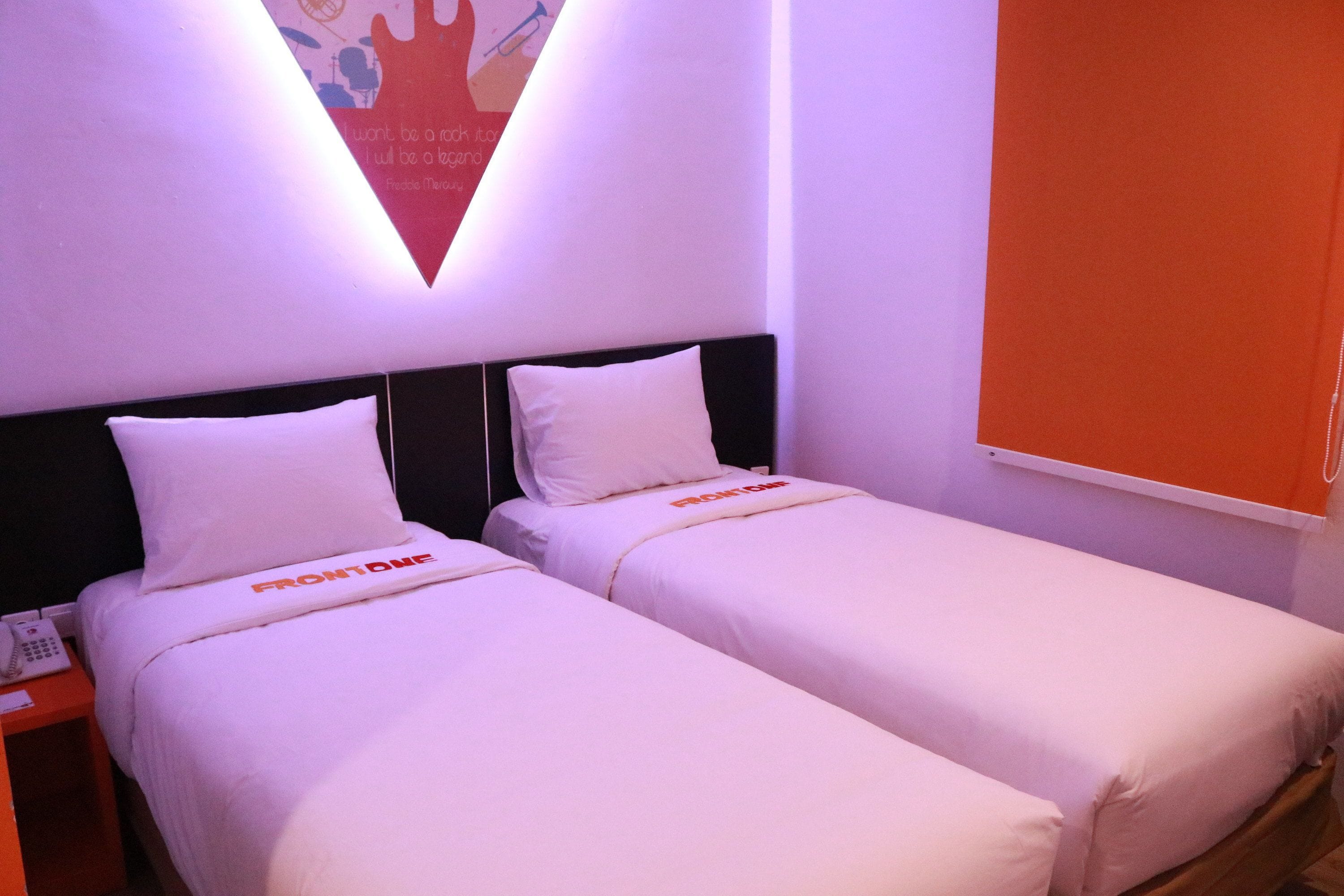 A hotel room with two single beds, each with a white bedspread and pillows, and a small bedside table with a phone.