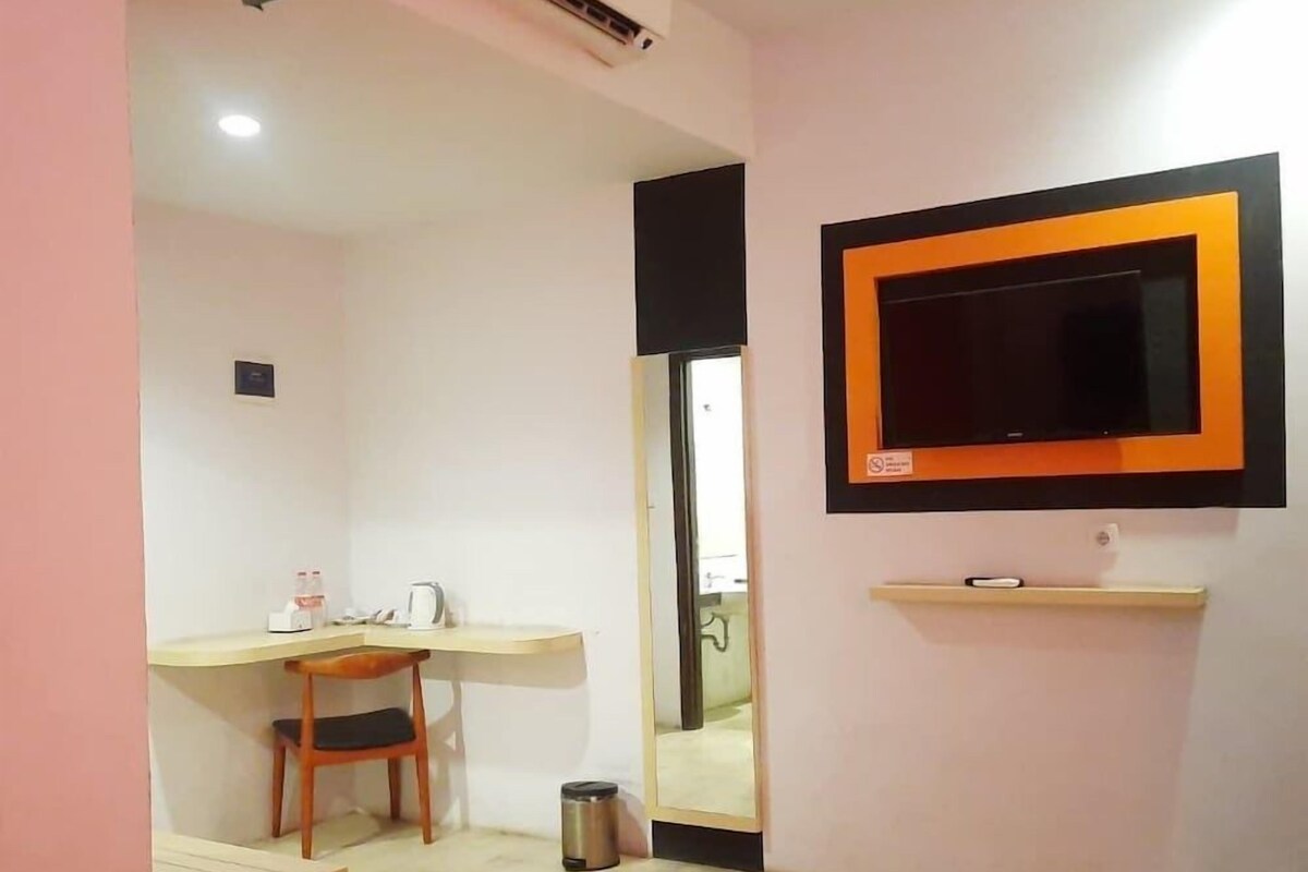 Una habitación de hotel con cama, escritorio, silla, televisor montado en la pared y aire acondicionado.