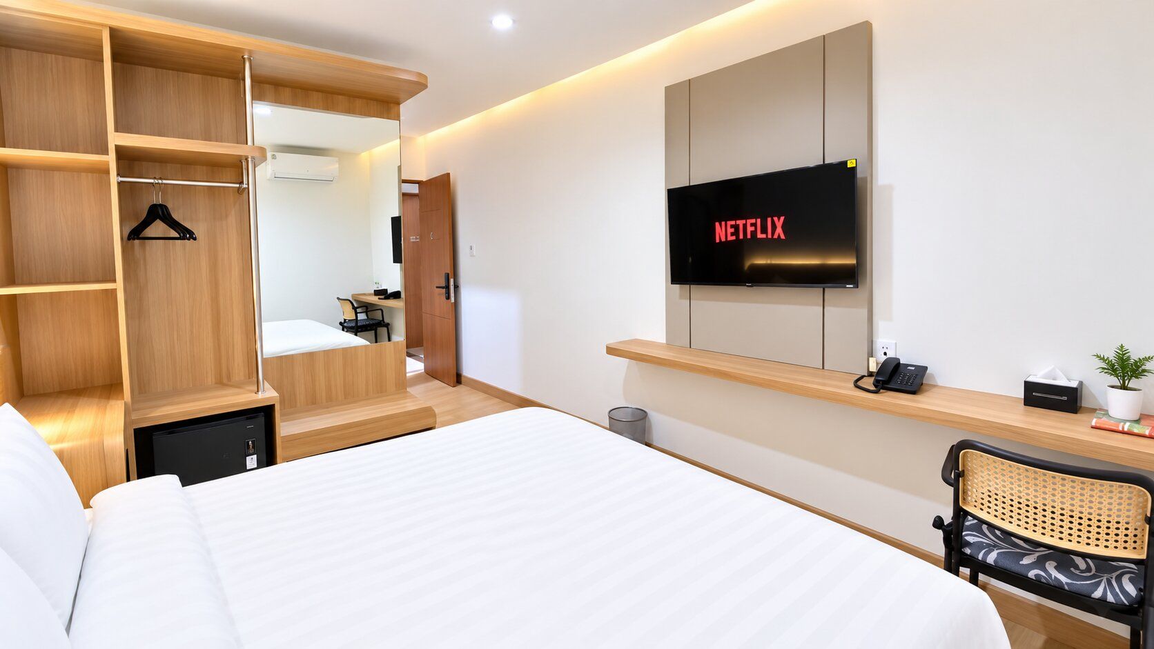 A hotel room with a bed, a wardrobe, a desk with a computer, a television, and a chair.