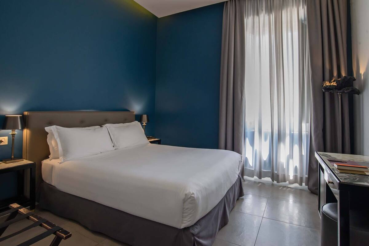 A hotel room with a large bed, a desk, and a chair.