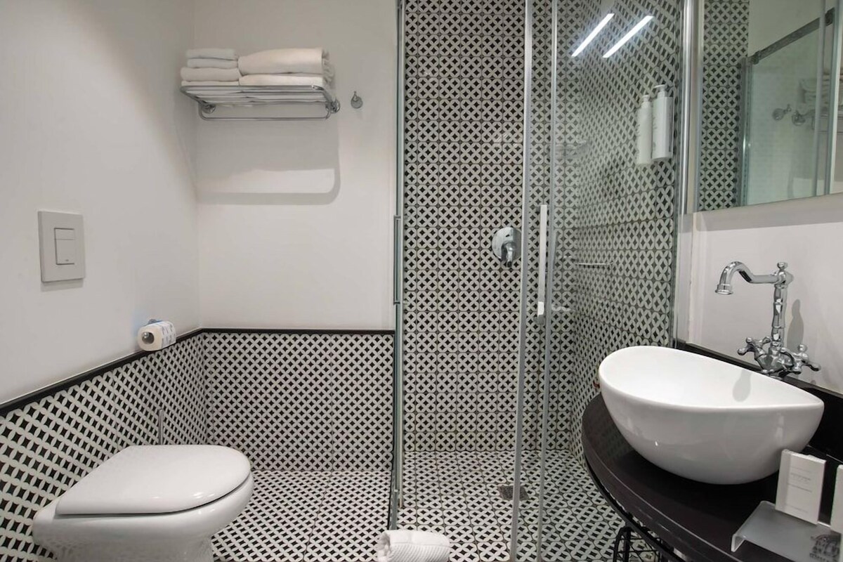Une salle de bain avec un carrelage noir et blanc, des toilettes blanches, une douche en verre et un lavabo blanc avec un miroir au-dessus.