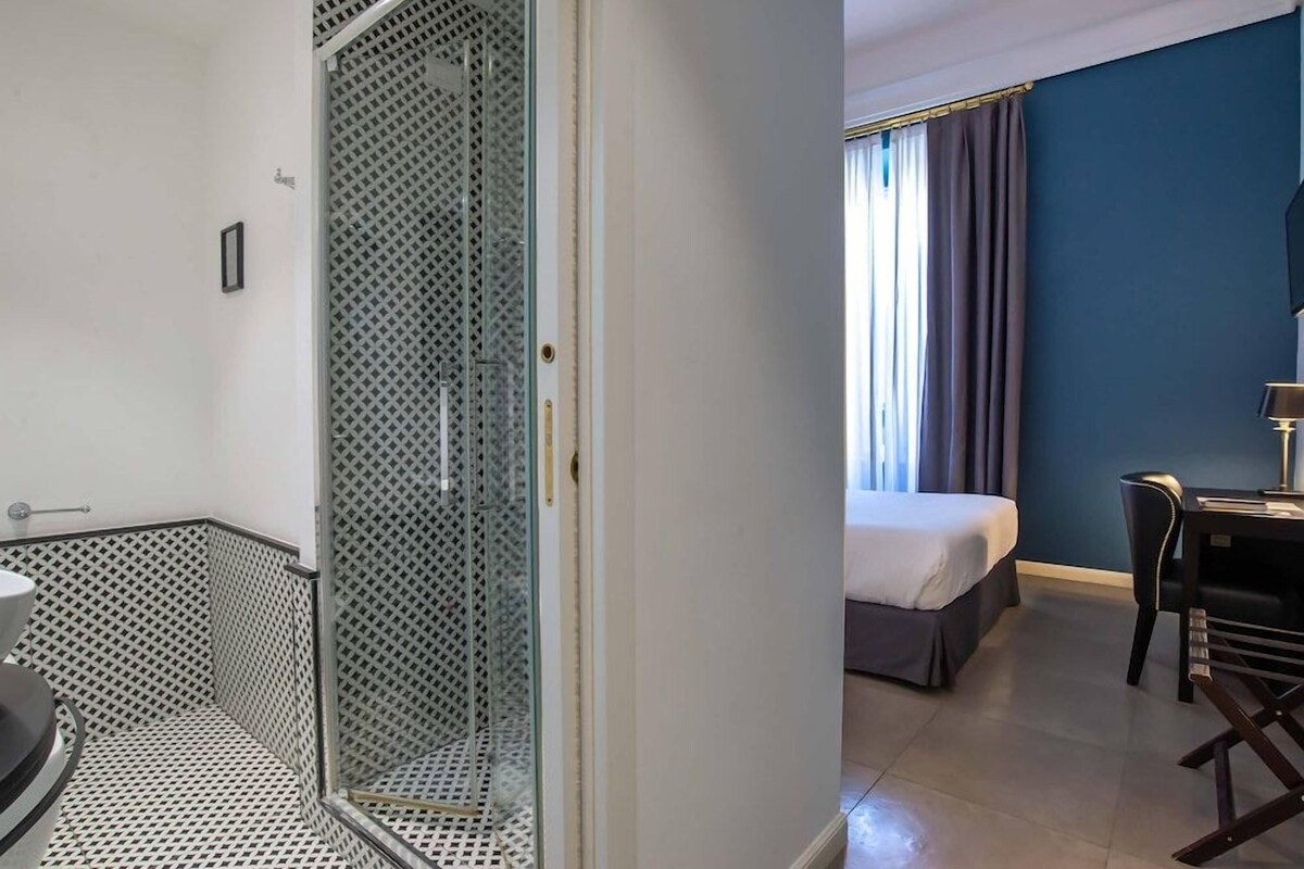 A hotel room with a shower, a bed, a desk, and a chair.