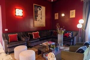 Een moderne woonkamer met een donkere bank, een glazen salontafel en een groot schilderij aan de muur.