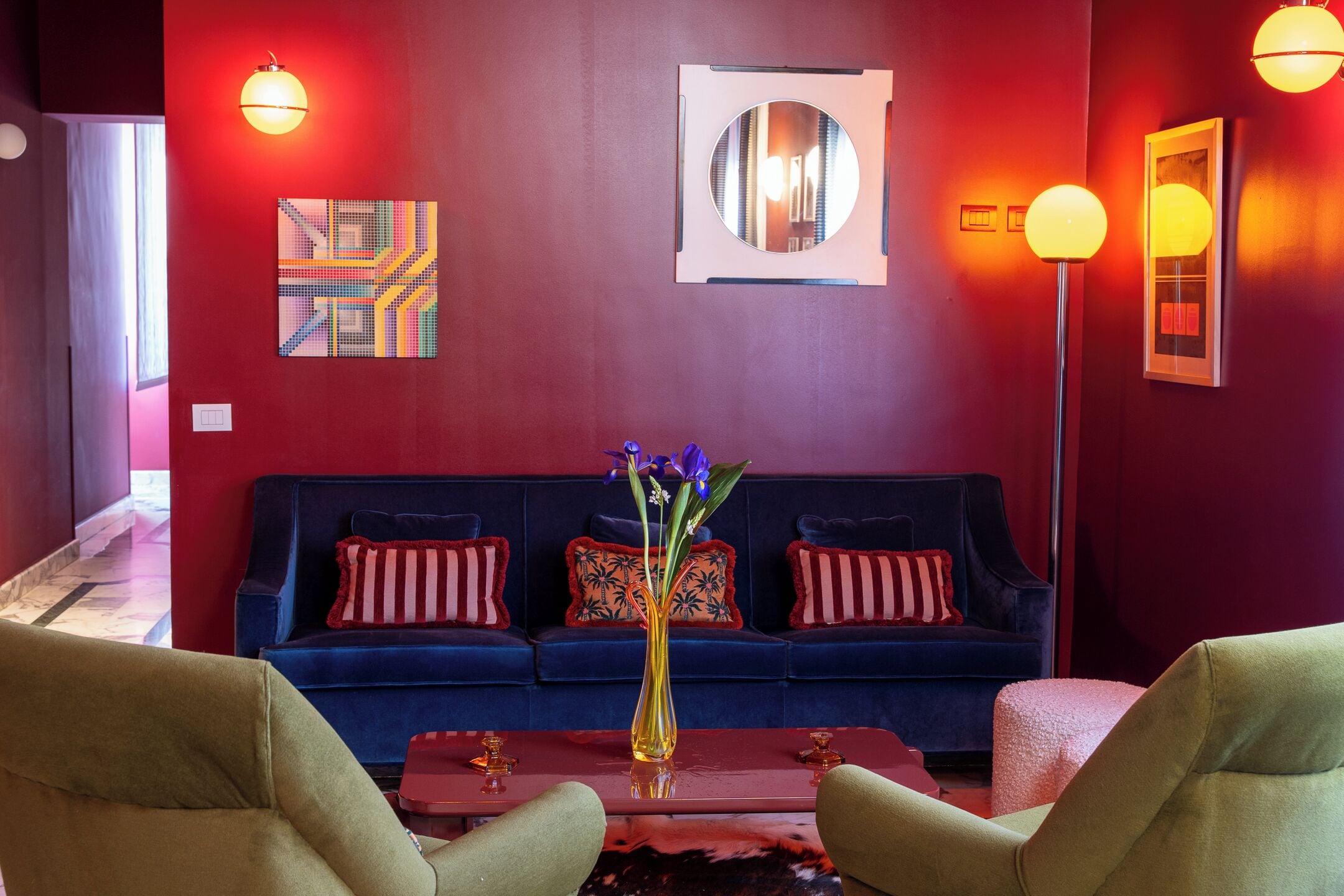 A room with a dark blue sofa, a vase with flowers, and a red wall.