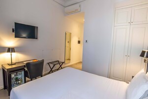 Hotellihuone, jossa on sänky, työpöytä lampun kanssa, televisio, minibaari ja vaatekaappi.