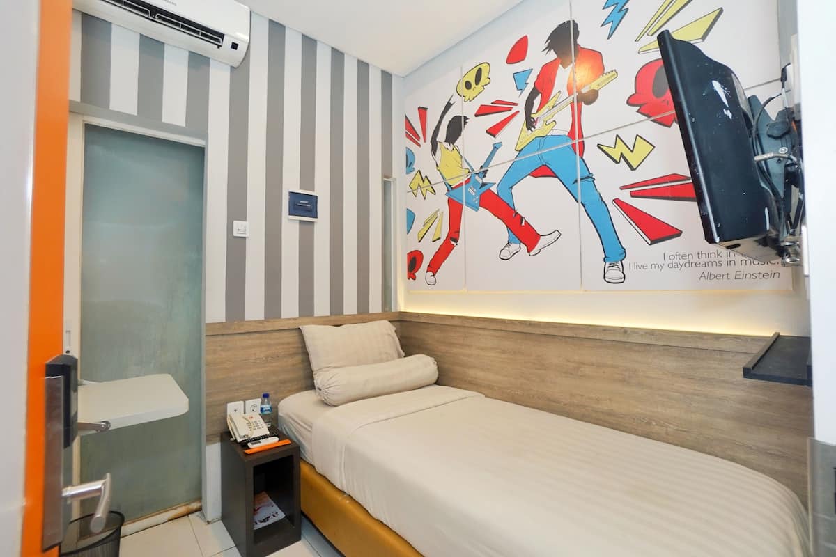 Una habitación de hotel con una cama, una mesita de noche pequeña con un teléfono, un televisor montado en la pared y una pared a rayas con un mural colorido.