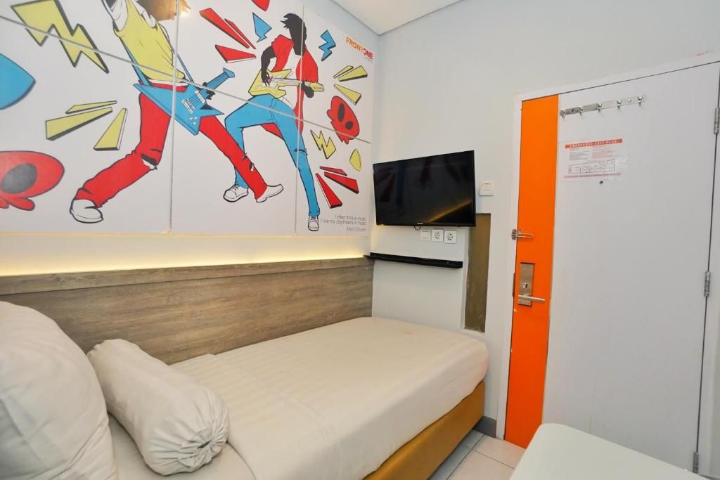 Habitació amb un llit individual, un panell de fusta al capçal, un televisor de pantalla plana al mur i una porta taronja.