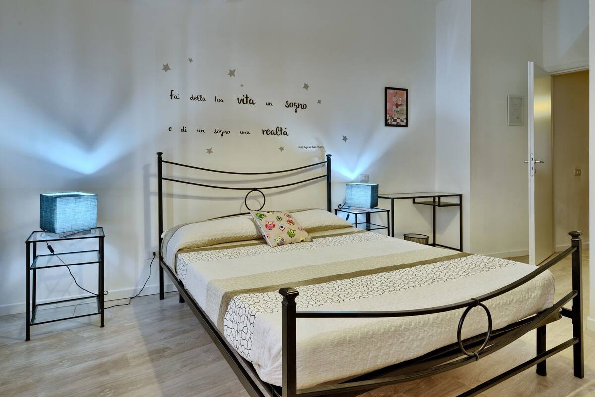 A neatly made bed with a patterned bedspread, two bedside tables with lamps, and a wall with a motivational quote.