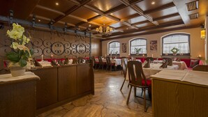 A restaurant with wooden booths, tables set with white tablecloths, and a stone floor. - Hotel Mondschein (Sesto)