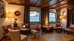 A cozy room with a stone floor, two armchairs with red cushions, a small round table, and a lamp. - Hotel Mondschein (Sesto)