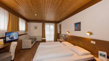 Ein Hotelzimmer mit Holzboden, einem Bett mit weißer Bettwäsche, einer Couch, einem Schreibtisch mit Fernseher und einem Nachttisch mit Lampe.