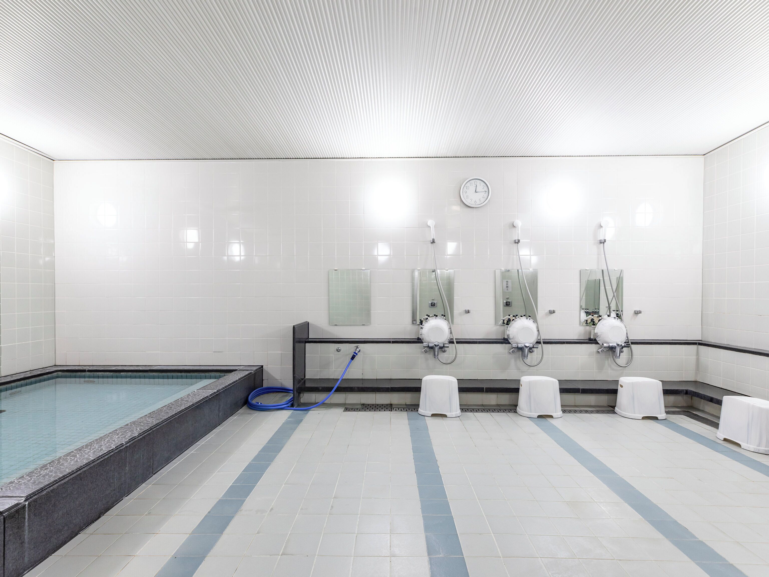 Ein helles, modernes Badezimmer mit weißen Fliesen, einem blauen Pool und mehreren Waschbecken mit Spiegeln.