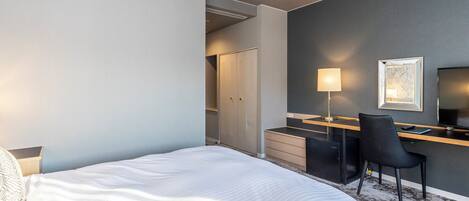 Una habitación de hotel con cama, escritorio, silla, lámpara y televisor.