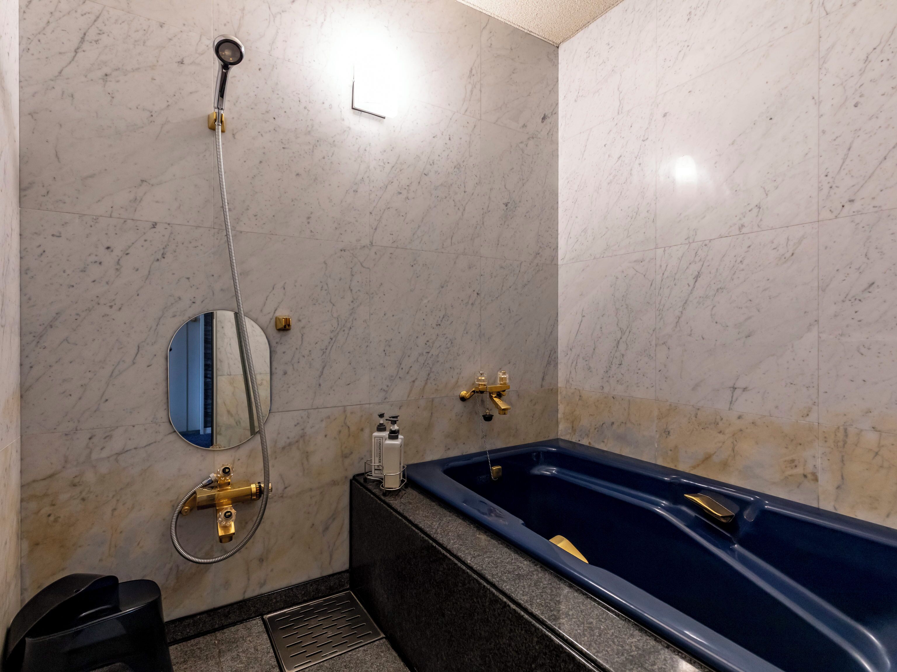 A bathroom with a marble floor, a bathtub, a shower, a sink with a faucet, and a mirror.