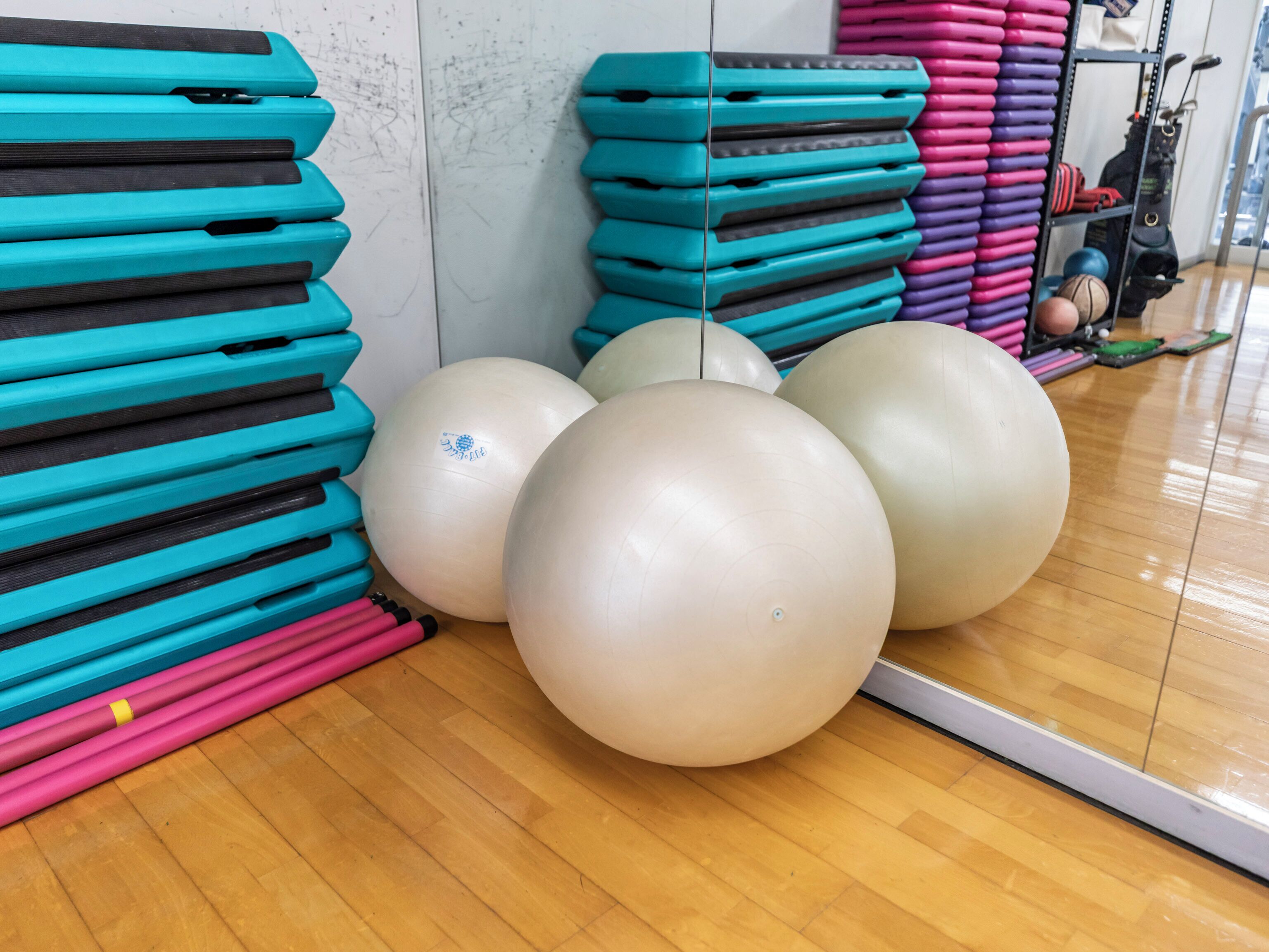 Un gimnasio con equipo de ejercicio, incluyendo colchonetas apiladas y pelotas de ejercicio grandes.