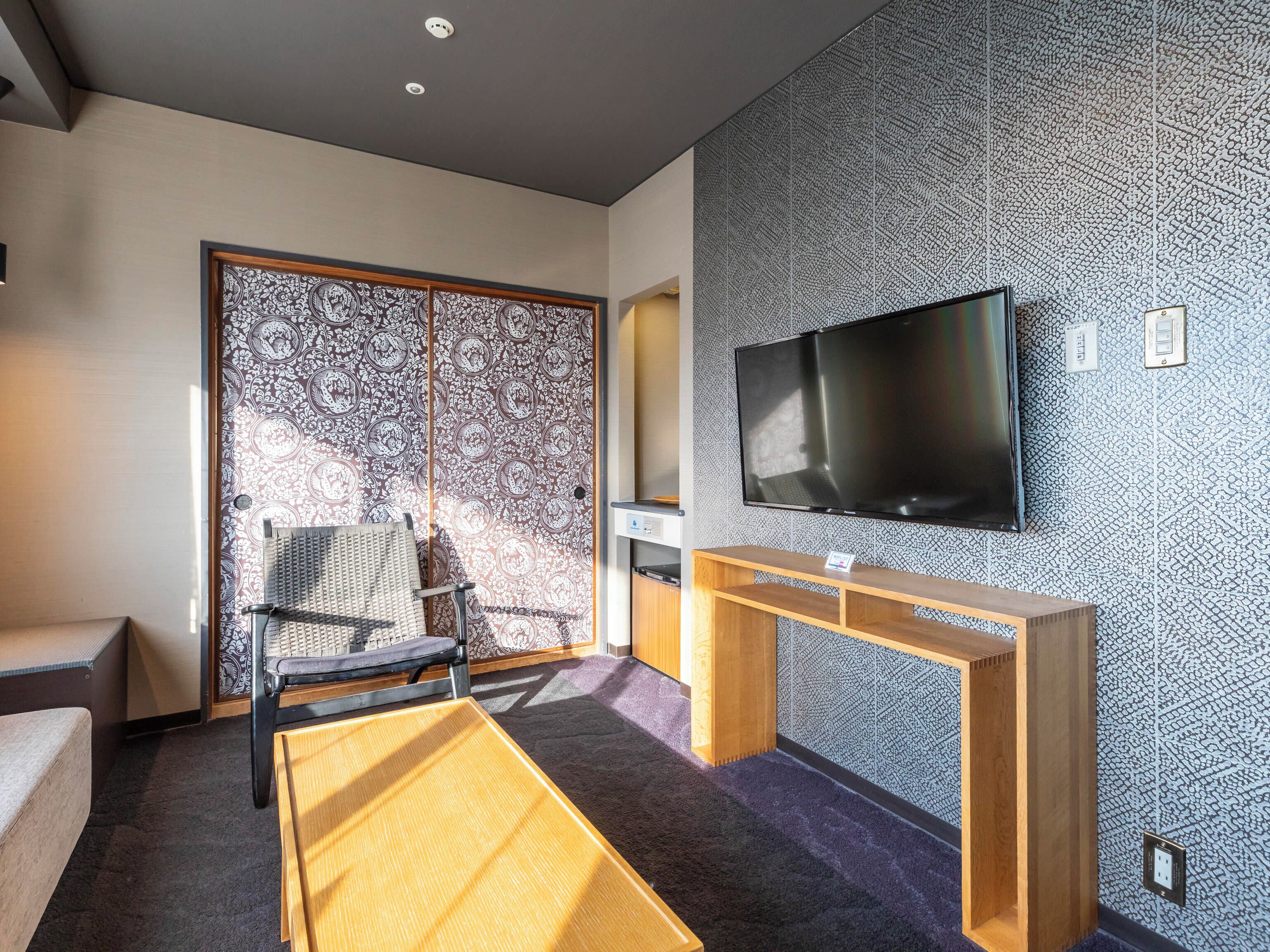 A modern hotel room with a large TV, a wooden console table, a patterned sliding door, and a sofa.