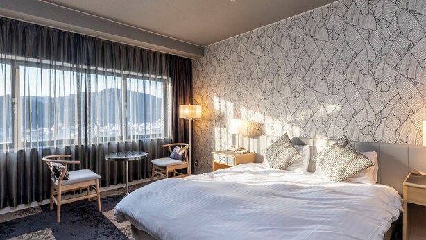 Una habitación de hotel con una cama grande, una silla, una mesita, una mesita de noche y una lámpara.