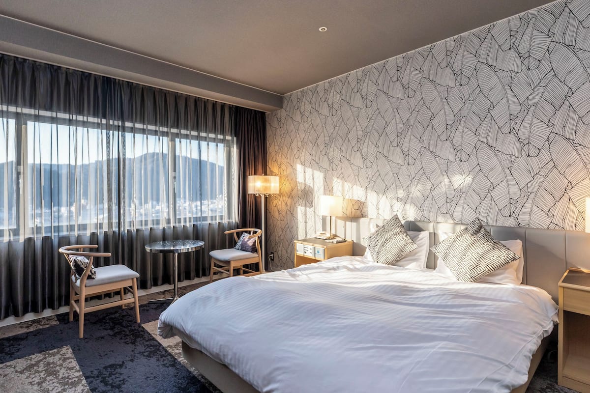 Ett hotellrum med en stor säng, en stol, ett litet bord, ett sängbord och en lampa.